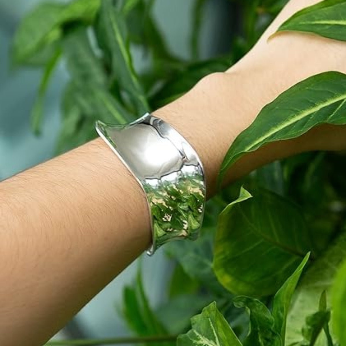 Silver bracelet on a wrist with green leaves in the background