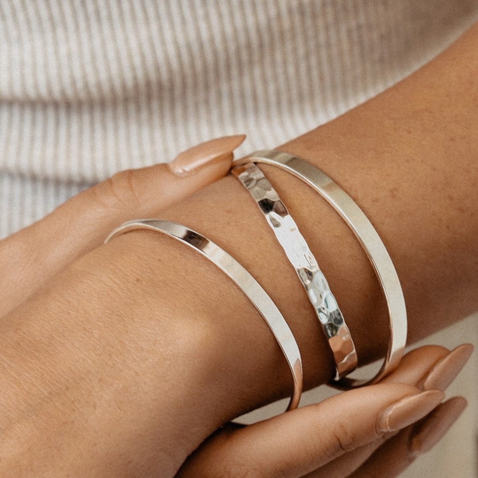 Close-up of a wrist wearing two silver bracelets on a neutral background